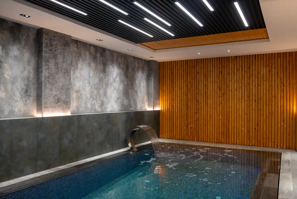 Subdued warm ambient lighting across stone poolside loungers and clear water